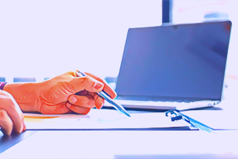 Close up person's hand, holding a pen. They are scanning over a document to check for accuracy